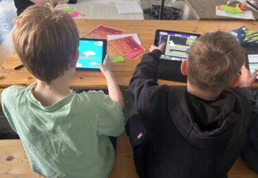 Zwei Kinder haben jeweils ein Tablet in der Hand und arbeiten in der Bloxels App ein einem eigenen Spiel.