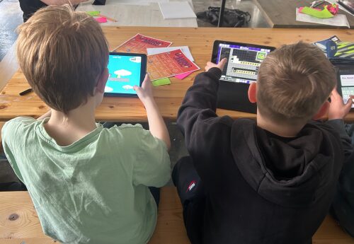 Zwei Kinder haben jeweils ein Tablet in der Hand und arbeiten in der Bloxels App ein einem eigenen Spiel.